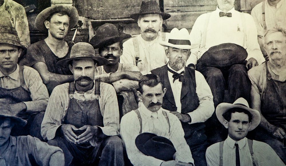На фотографии Джек Дэниэл в белой шляпе, фото сделано на его винокурне в Теннесси в конце 1800-х годов. Человек справа от него мог быть сыном Неариса Грина, раба, который помогал Дэниелу научиться делать виски.